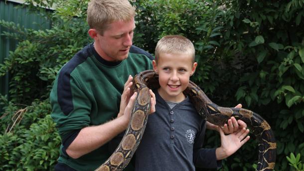 A boy holding a cobra and a man standing next to him