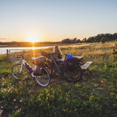 Kvinne slapper av ved et bord og en benk, midt på et jorde, og beundrer soloppgangen over vannet ved knudshoved på Fyn